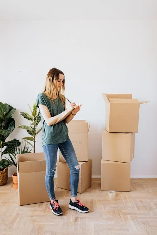 a woman writing on a notepad in a room with boxes